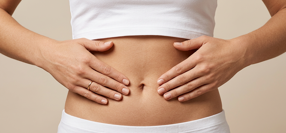 Primo piano sulle mani di una donna poggiate sulla pancia in un gesto di automassaggio per alleviare la digestione su sfondo beige neutro